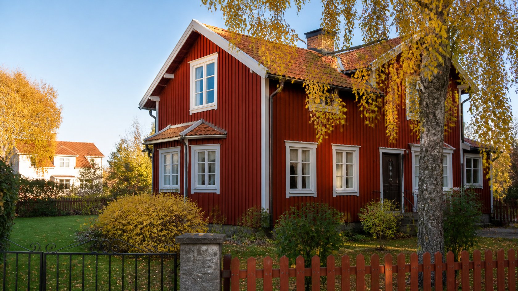 Röd svensk trävilla med vita fönster och gul björk i höstljus – omvärdering av bostad